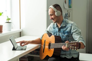 40 yaşında bir adam evde gitar çalıyor ve dizüstü bilgisayar kullanıyor. Yüksek kalite fotoğraf