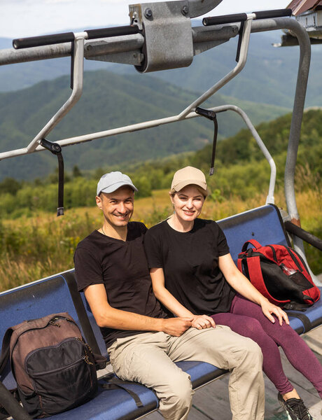 Man and a woman riding on the lift down the scenic Mountain during summer. Green tree forest surrounds the escalator