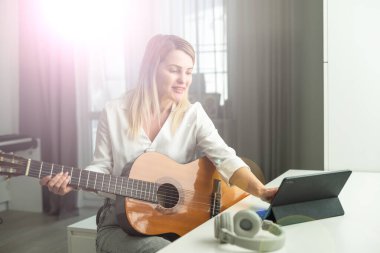 Kablosuz kulaklıklı, dizüstü bilgisayarla otururken akustik müzik aleti kullanan sakin genç bir kadın. Yüksek kalite fotoğraf