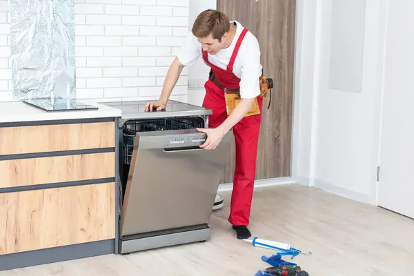Full length of repairman repairing dishwasher with screwdriver in kitchen