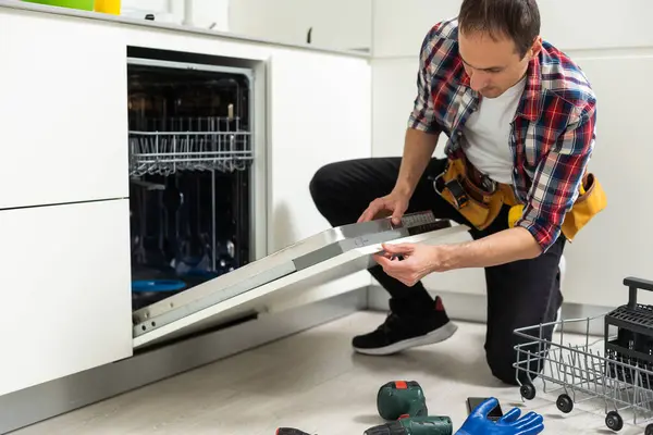View Of Man In Overall Repairing Dishwasher In Kitchen. High quality photo