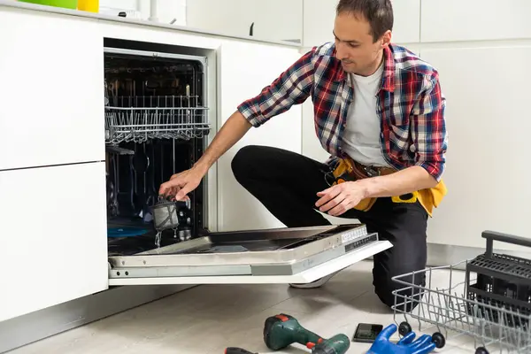 Professional worker repairing the dishwasher in the kitchen. High quality photo