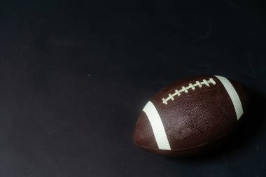 Stüdyo çekiminde Amerikan futbolu. Top, hafifçe aydınlatılmış siyah bir zemin üzerinde. Yüksek kalite fotoğraf