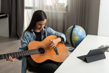 Genç kız online dersleri kullanarak evde gitar çalmayı öğreniyor. Uzaktan hobi müzik eğitimi akustik gitar. Uzayı kopyala Yüksek kalite fotoğraf