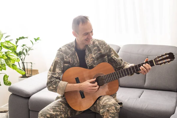 Cheerful smiling young military man wearing khaki uniform holding guitar. High quality photo