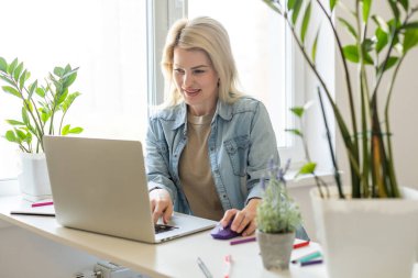Çekici mutlu genç kız öğrenci ders çalışıyor, masada oturuyor, dizüstü bilgisayar kullanıyor, görüntülü sohbet ediyor, el sallıyor..