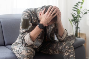 Kafkasyalı ciddi bir askerin portresi. Kamuflaj üniforması ve şapka takıyor. Kanepede oturuyor ve yüzünde depresif bir ifade var. Yüksek kalite fotoğraf