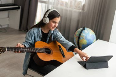 Genç kız online dersleri kullanarak evde gitar çalmayı öğreniyor. Uzaktan hobi müzik eğitimi akustik gitar. Uzayı kopyala Yüksek kalite fotoğraf
