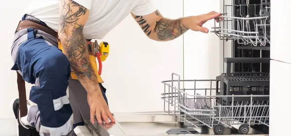 man repairing dishwasher. Male hand with screwdriver installs kitchen appliances, close up.