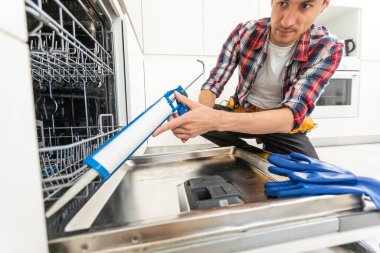 Mutfakta alet çantasıyla bulaşık makinesini inceleyen bir tamirci. Yüksek kalite fotoğraf