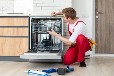 Bulaşık makinelerinin tamiri. Tamirci mutfakta bulaşık makinesini tamir ediyor..
