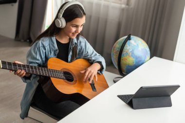 Uzun saçlı, gitar çalan, evde oturan güzel bir genç kız. Melodiyi çalışıyorum. Ev eğlencesi, hobiler, kendini geliştirme. Yüksek kalite fotoğraf