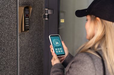 Kadın, evinin kapısını açmak için akıllı telefon kullanıyor. Yüksek kalite fotoğraf