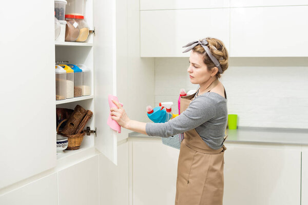 Молодая женщина занимается домашними делами. Женщина с инструментами для чистки. Женщина в резиновых защитных жёлтых перчатках, держит тряпку и моющее средство для бутылок. It never too late to spring clean.