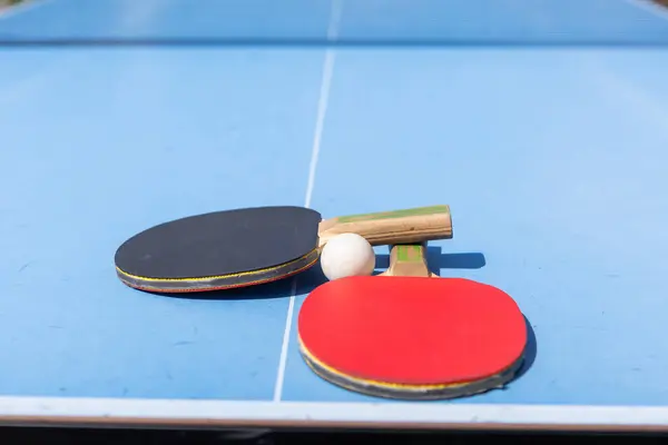 Red and black Table Tennis Paddles and ball on the blue table tennis table with net. Ping Pong concept with copy space. High quality photo