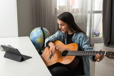 Uzun saçlı, gitar çalan, evde oturan güzel bir genç kız. Melodiyi çalışıyorum. Ev eğlencesi, hobiler, kendini geliştirme. Yüksek kalite fotoğraf