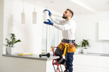 Elektrikçi tavan lambasına ampul yerleştiriyor.