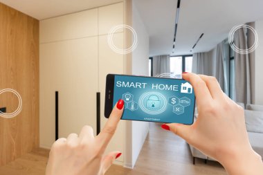 Akıllı ev telefonu, akıllı ev telefonu uygulama arayüzü cep telefonu ekranında, modern apartmandaki tüm ev sistemini telefonla kontrol eden genç bir kadın, konsept internet.