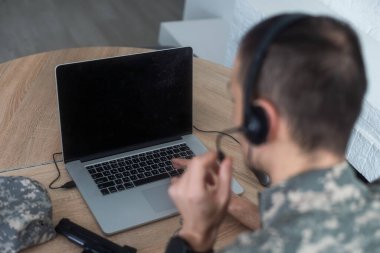 Kulaklıklı gülümseyen asker mutfak masasında dizüstü bilgisayar kullanıyor. Yüksek kalite fotoğraf