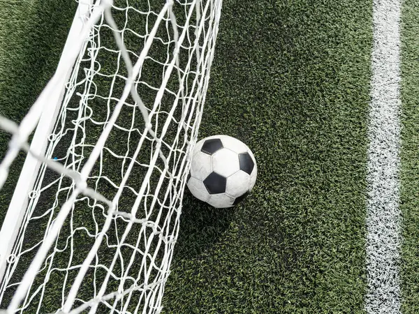 Soccer football in Goal net with green grass field. High quality photo