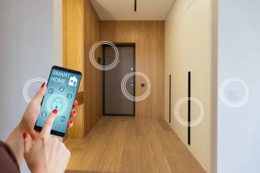 Akıllı ev telefonu, akıllı ev telefonu uygulama arayüzü cep telefonu ekranında, modern apartmandaki tüm ev sistemini telefonla kontrol eden genç bir kadın, konsept internet.