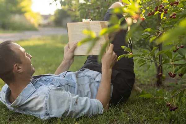 Genç adam çimenlerde uzanıyor, rahatlıyor ve kitap okuyor..
