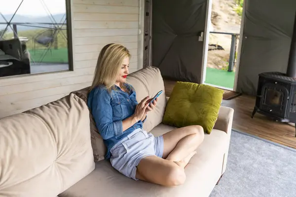 stock image Happy young caucasian woman relax on comfortable couch at home texting messaging on smartphone, use cellphone, browse wireless internet on gadget, shopping online from home.