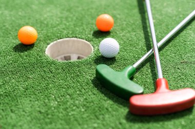 Mini-golf clubs and balls of different colors laid on artificial grass