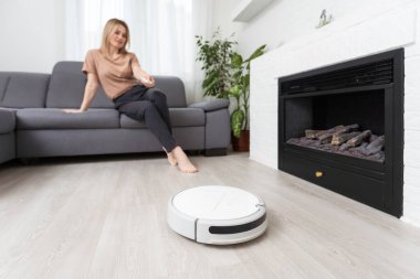 Kadın kanepede dinlenirken robot süpürgesi odayı temizliyor..
