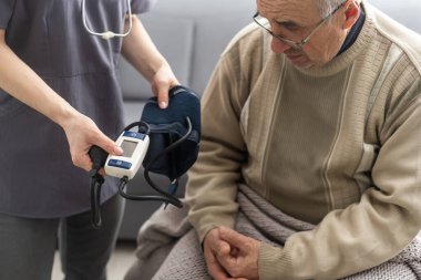 Hemşire, klinikteki yaşlı hasta bir erkek hastanın yüksek tansiyonunu ölçüyor. Doktor hipertansiyonu olan yaşlı bir adamın kan basıncını ölçüyor. Sağlık hizmetleri kavramı.