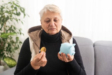 Domuzlu para kutusu tutan yaşlı kadının yakın çekimi. Kıdemli kadın elleri domuz kumbarası tutuyor. Yaşlılık için para biriktirme kavramı