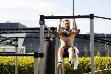 Kaslı yakışıklı adam şehir merkezindeki sokak sporları sahasındaki makinelerde üst vücut eğitimi veriyor.