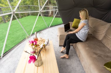 Kubbe kampında dizüstü bilgisayar kullanarak internette sohbet eden mutlu genç bir kadın. Glamping tatil konsepti.