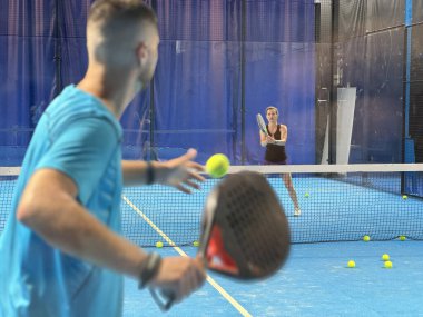 Bir koç olarak Padel tenis eğitimini güçlendirmek, sahadaki genç bir kadına ustalıkla eğitim verir, beceri geliştirmeyi teşvik eder ve olumlu bir öğrenme ortamı sağlar. Yüksek kalite fotoğraf