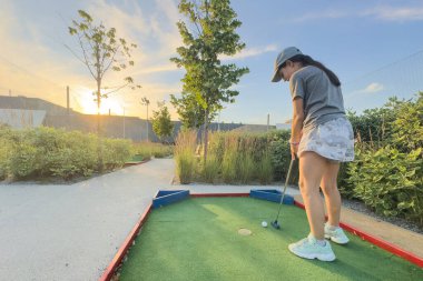 Mini Golf - gün batımında yeşil çimlerde golf oynayan kız. Yüksek kalite fotoğraf