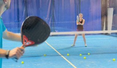 Bir koç olarak Padel tenis eğitimini güçlendirmek, sahadaki genç bir kadına ustalıkla eğitim verir, beceri geliştirmeyi teşvik eder ve olumlu bir öğrenme ortamı sağlar. Yüksek kalite fotoğraf