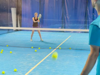 Bir koç olarak Padel tenis eğitimini güçlendirmek, sahadaki genç bir kadına ustalıkla eğitim verir, beceri geliştirmeyi teşvik eder ve olumlu bir öğrenme ortamı sağlar. Yüksek kalite fotoğraf