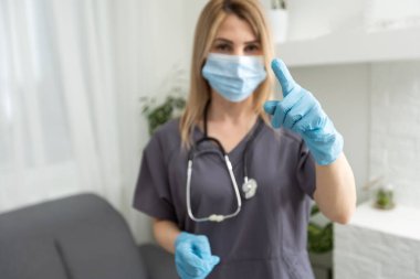 Yorgun kadın doktor. Koronavirüs. Koruyucu maskeli ve eldivenli genç bayan doktor parmak gösteriyor.