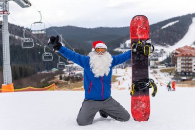 Kayak merkezinde kar kayağı yapan Noel Baba şapkalı bir adam.