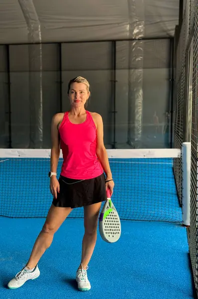 Padel kortunda raketi olan, gülümseyen ve kameraya bakan genç bir kız. Yüksek kalite fotoğraf