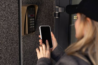 Bir kadın akıllı telefon kullanarak giriş kapısına akıllı kilit takıyor. Anahtarsız erişimi olan akıllı elektronik kilitler kullanma kavramı. Yüksek kalite fotoğraf