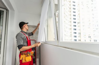 Balkonda su geçirmez silikon caulk kullanarak pencere ile süsleme arası çatlakları kapatan tulum giyen genç bir adam. Yüksek kalite fotoğraf