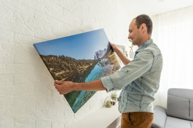 Galeri ambalajı ve kuru çim iç dekorlu tuval baskısı. Kadın fotoğrafçılığı beyaz duvara asıyor. Ellerinde Fransa 'nın Biarritz şehrindeki adanın resmi olan bir tuval var. Yüksek kalite fotoğraf