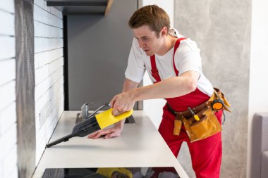 Profesyonel temizlik servisinden bir adam elektrikli süpürgeyle mutfak mobilyalarını temizliyor. Tamirattan sonra odayı hazırla. Temizlik ve ev konsepti