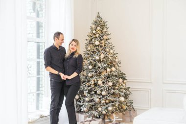 Mutlu Noeller ve mutlu yıllar. Güzel bir çift yeni yılı birlikte beklerken ellerinde hediye kutusuyla güzel bir Noel ağacının yanında kucaklaşıyorlar. Yüksek kalite fotoğraf