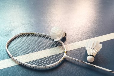 Krem beyazı badminton servis aleti ve kapalı badminton kortunun karanlık zemininde neon ışıklı raket, kopyalama alanı, yumuşak ve seçici odaklanma. Yüksek kalite fotoğraf