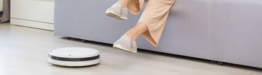 Yerleri temizlemek için otomatik süpürge kullanan genç bir kadın makine ev işi robotu kontrol ediyor..