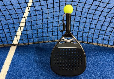Açık havada mavi kortta kürek ağının arkasında sarı top var. Padel tenisi bir raket oyunudur. Profesyonel spor konsepti. Yüksek kalite fotoğraf