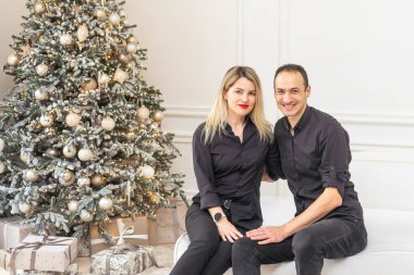 Mutlu Noeller ve mutlu yıllar. Güzel bir çift yeni yılı birlikte beklerken ellerinde hediye kutusuyla güzel bir Noel ağacının yanında kucaklaşıyorlar. Yüksek kalite fotoğraf