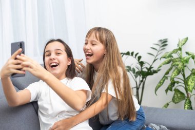 İki tatlı beyaz sarışın kız kardeş ellerinde cep telefonuyla gülüyorlar. Yüksek kalite fotoğraf